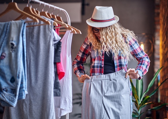 positive-blonde-female-black-eyeglasses-chooses-fashionable-clothes-coat-rack.jpg